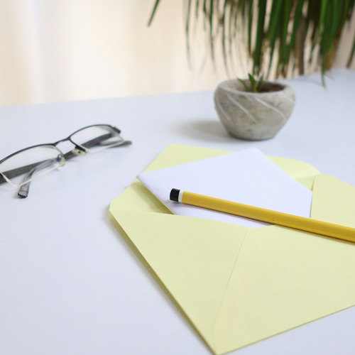 Crayon, lunettes, enveloppe et plante sur une table.